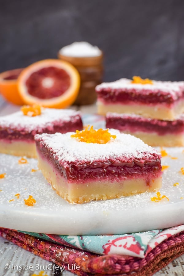 Squares of orange bars topped with powdered sugar on a white board.