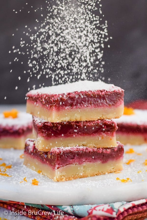 A stack of three blood orange bars with powdered sugar being sprinkled on top.