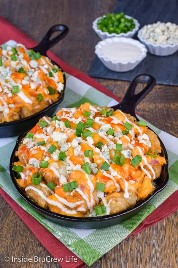 A cast iron skillet full of tater tots, buffalo chicken, and cheese.