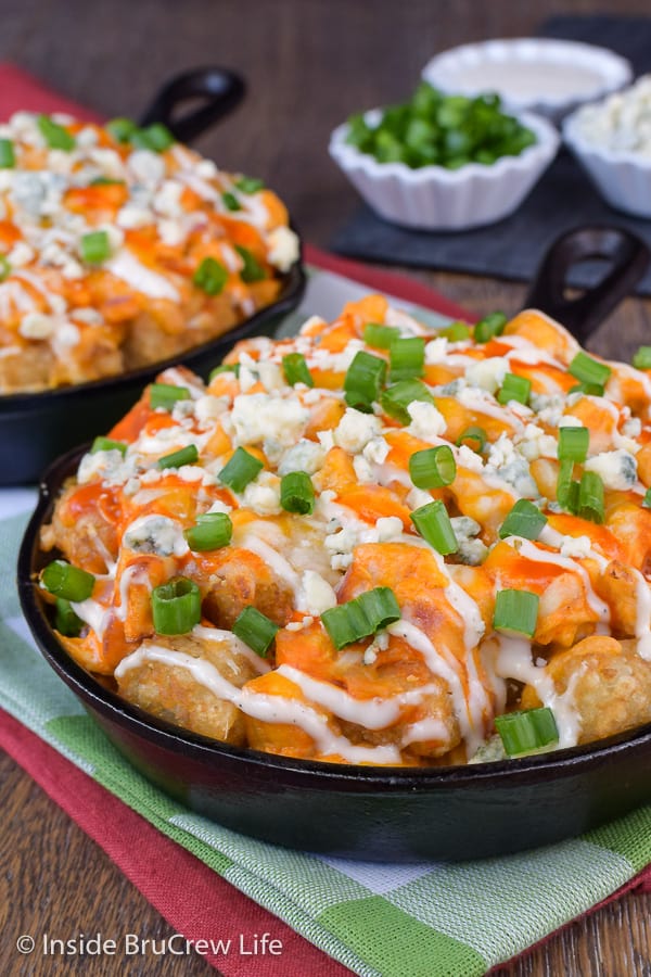 A cast iron skillet with tater tots, buffalo chicken, and other toppings.