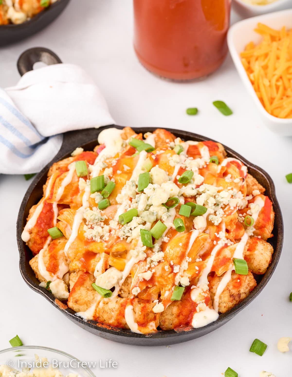 A black pan filled with cheesy tater tots and buffalo chicken.