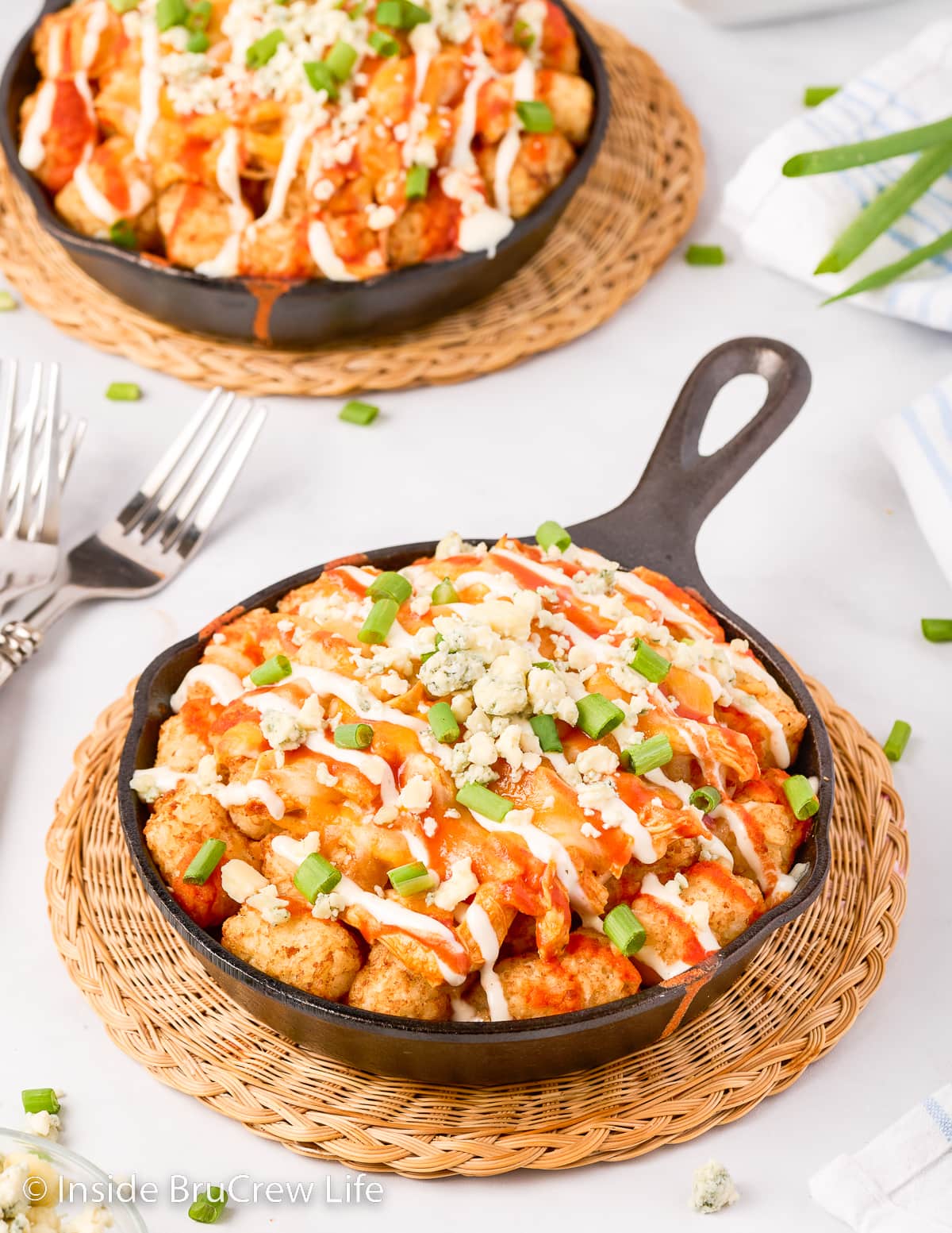 Two black pans filled with cheesy tater tots and buffalo chicken.