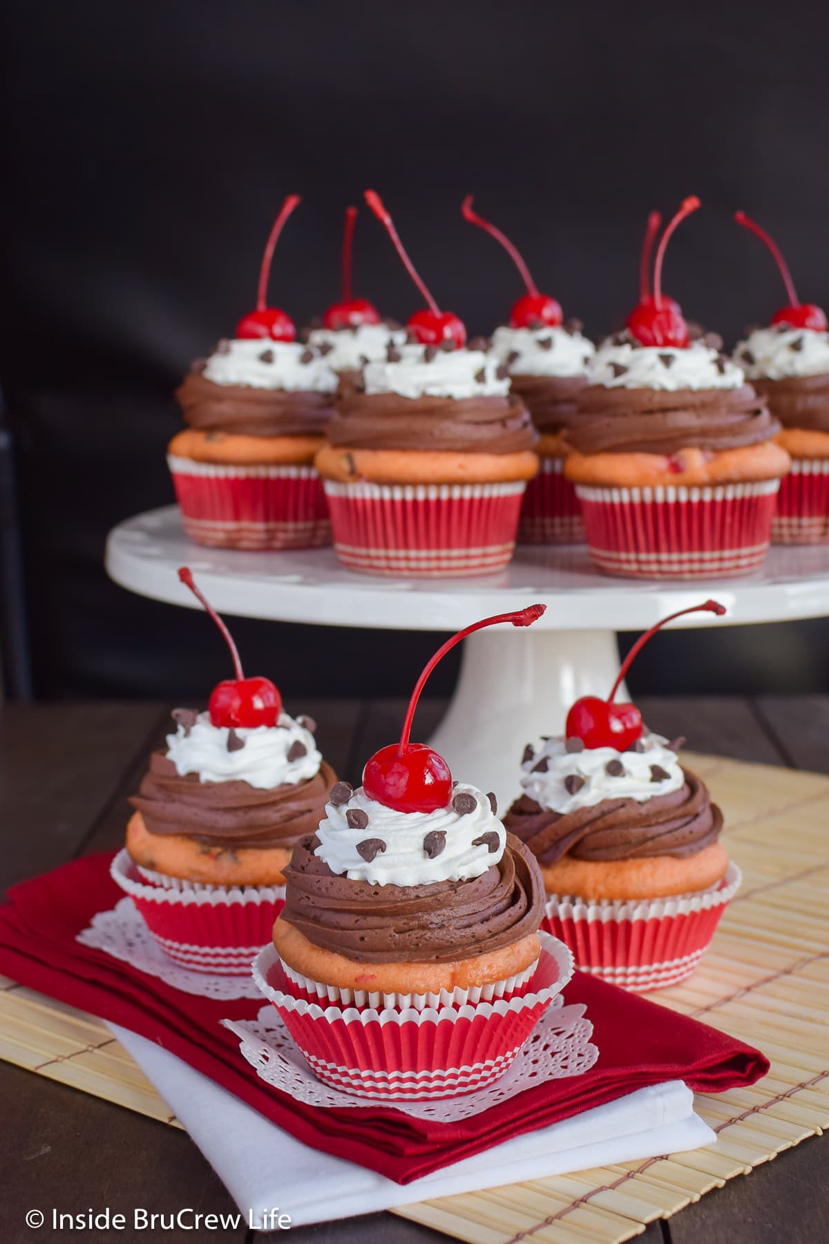 Frosted cupcakes topped with a cherry on a cake plate.