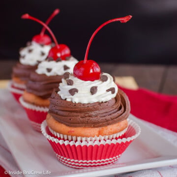 Three frosted cupcakes with cherries on a white tray.