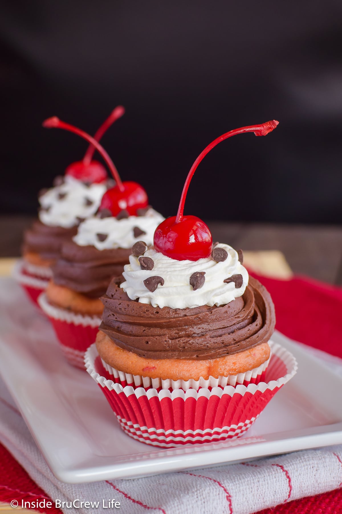 Three frosted cupcakes with cherries on a white tray.