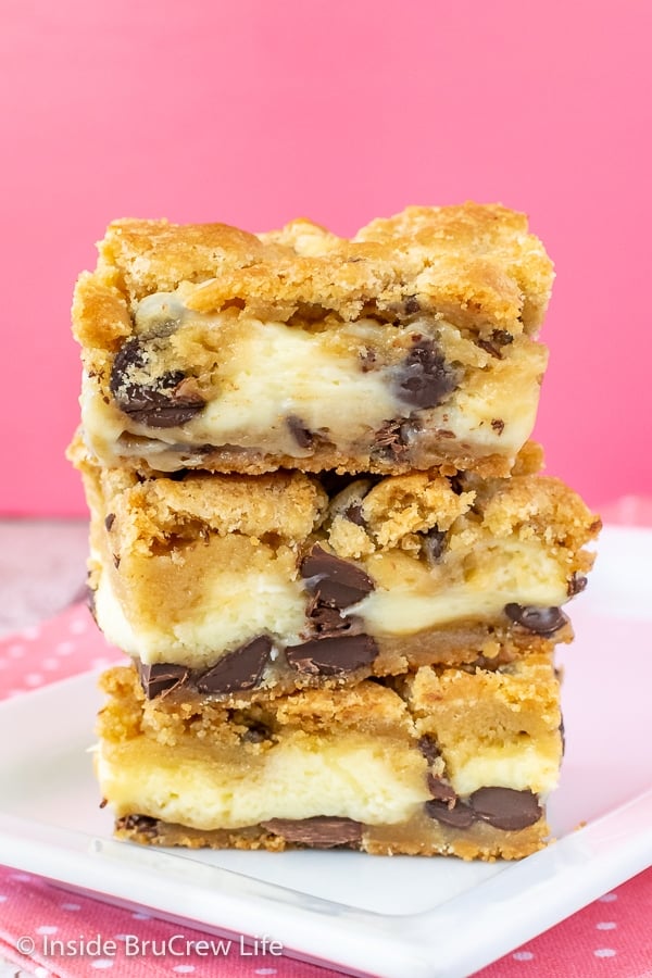 A stack of three chocolate chip cheesecake cookie bars on a white plate with a pink background.