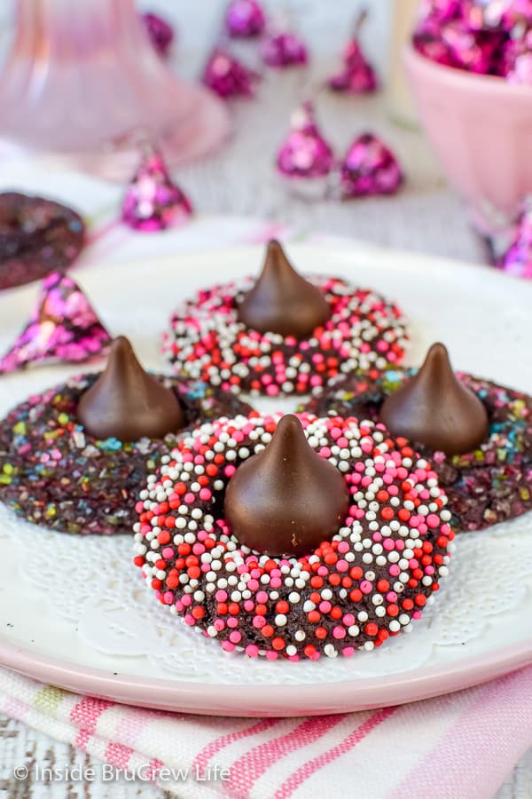 A white plate of chocolate cookies covered in sprinkles and topped with a Hershey kiss.