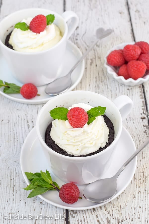 Two white cups with a microwave lava cake, whipped cream, and raspberries.