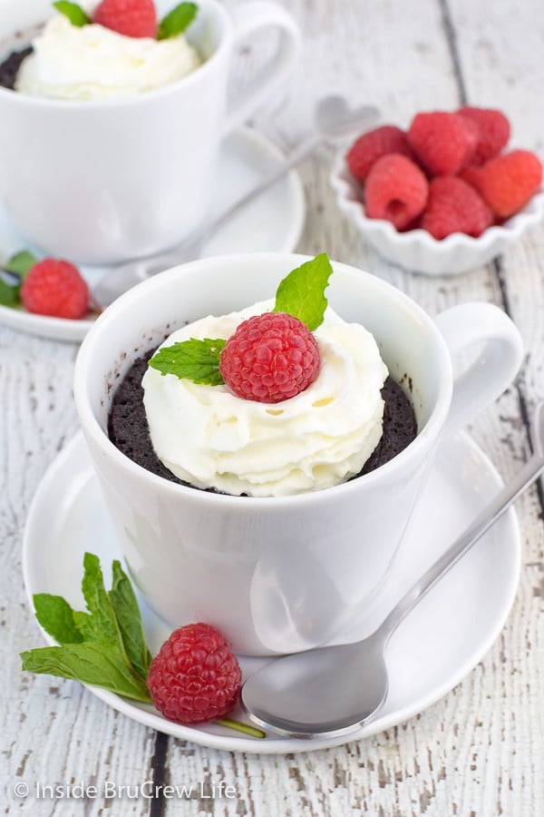 Two white cups with chocolate lava cake topped with whipped cream and a raspberry.