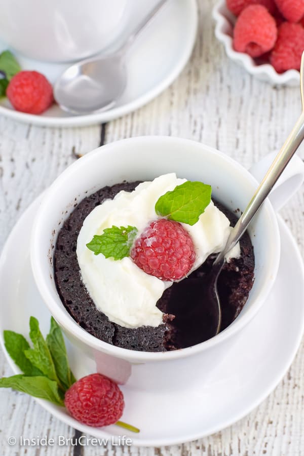 Overhead picture of a white cup with chocolate lava cake, whipped cream, and a raspberry.