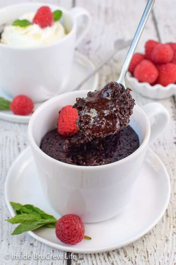 A white cup with a chocolate lava cake in it and a spoon lifting out a gooey bite.