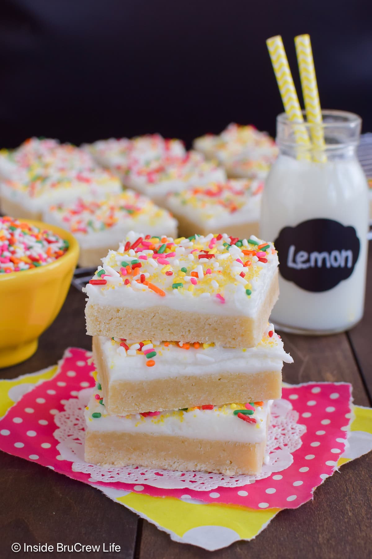 A stack of three frosted lemon cookie bars on a pink paper.