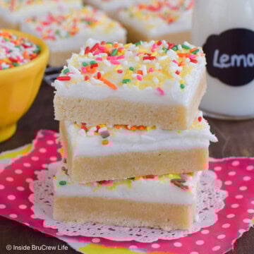 A stack of three frosted lemon cookie bars on a pink paper.