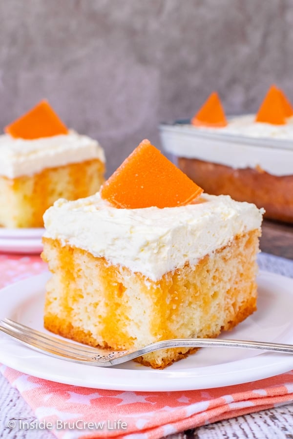 Two white plates with pieces of orange creamsicle cake topped with vanilla mousse frosting and orange slices