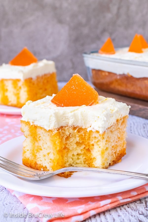 Two white plates with pieces of orange creamsicle cake topped with vanilla pudding frosting and orange slices on them