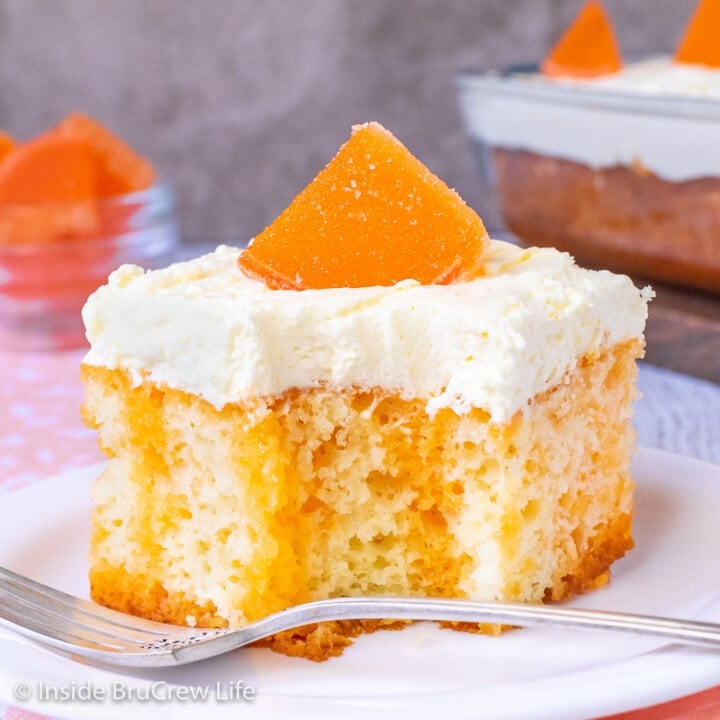 A white plate with a piece of orange poke cake with pudding frosting on it