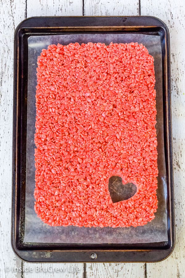 A pan of pink rice krispie treat with a heart shape cut out of it.