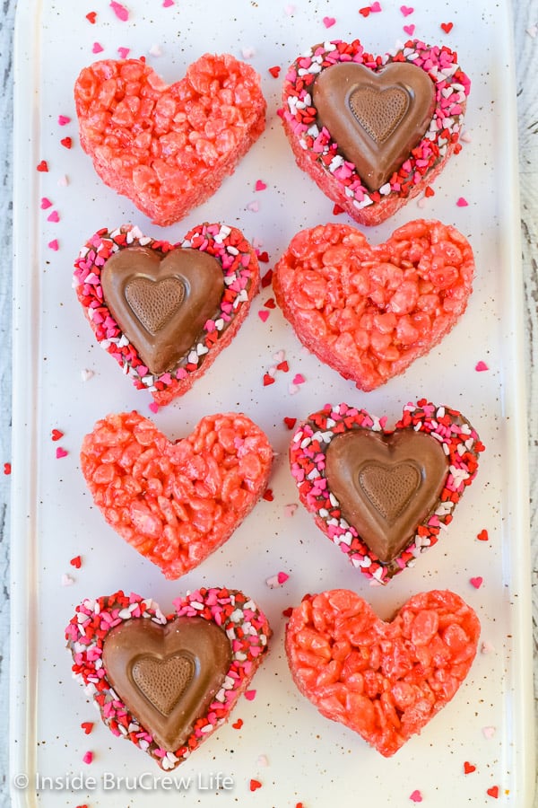 A pan of pink rice krispie treats with chocolate hearts and candy on them.