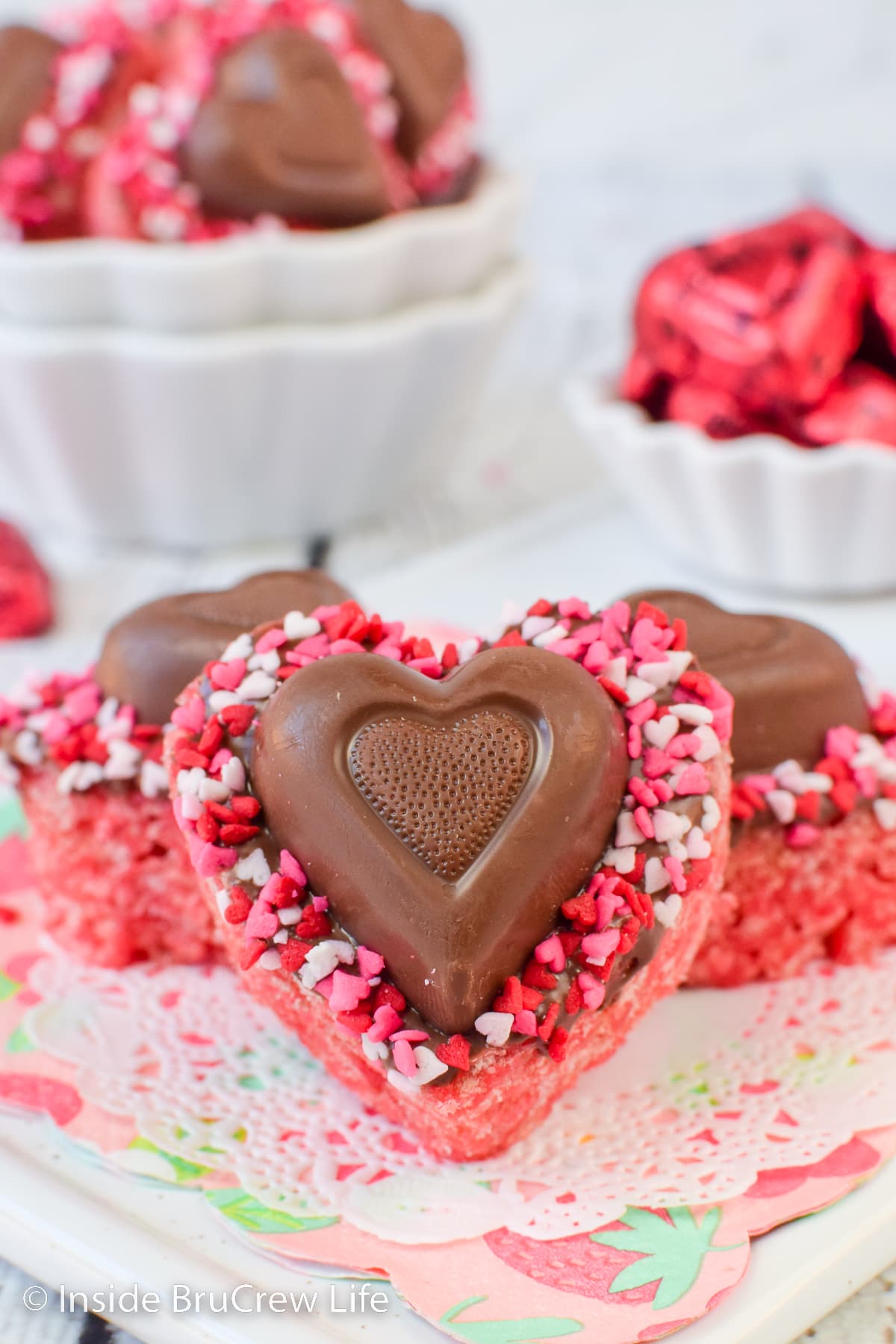 Pink rice krispie treats cut into hearts and topped with a chocolate heart on a white tray.