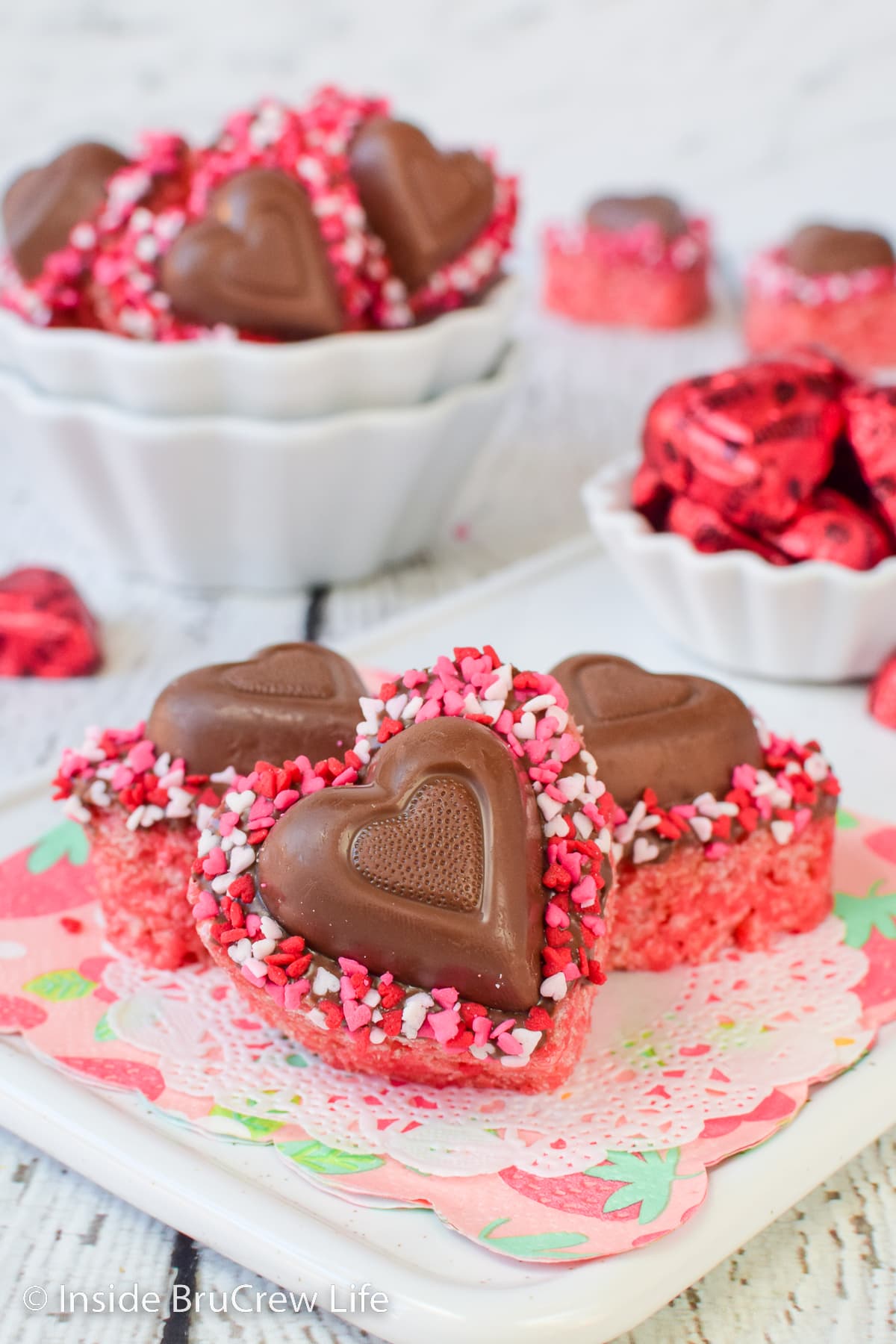 Pink rice krispie treat hearts with chocolate hearts on a white tray.