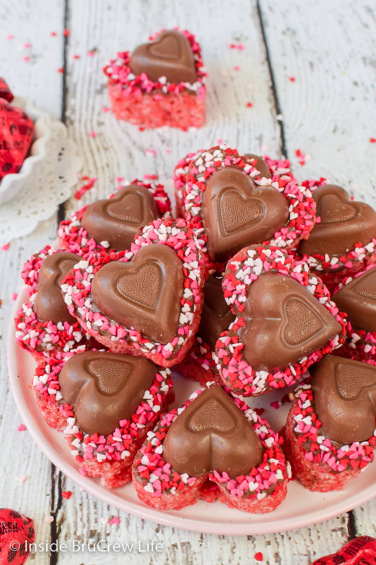 Pink rice krispie treat hearts with chocolate hearts on a white plate.