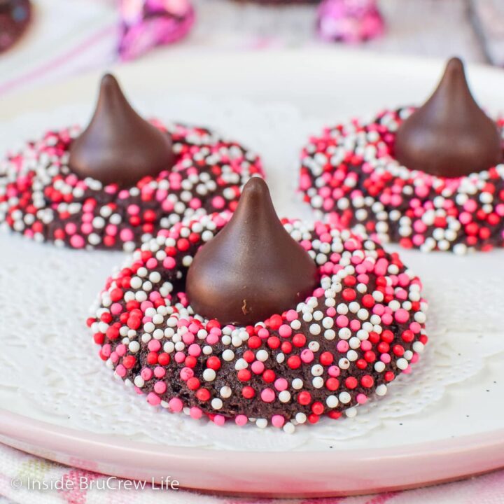 A white plate with three chocolate sprinkles cookies topped with Hershey kisses.
