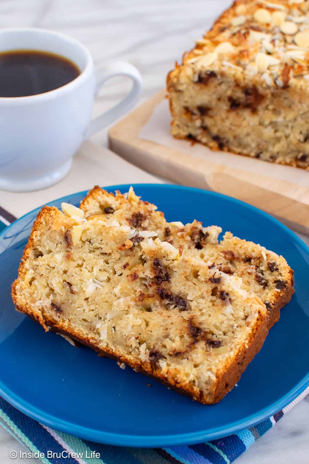 Two slices of almond joy banana bread on a blue plate with the loaf behind it.