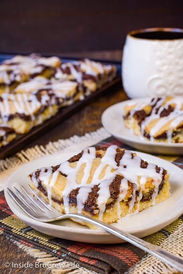 Two cream plates with a square of banana nutella snack cake on it and a pan of banana cake behind it