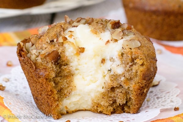 A carrot cheesecake muffin with a bite out of it on a white paper.