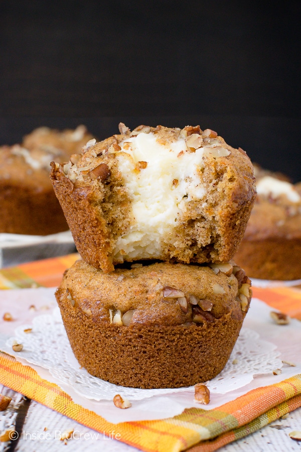Two carrot cake muffins stacked on top of each other on an orange towel with a bite taken out of the top one showing the cheesecake center.