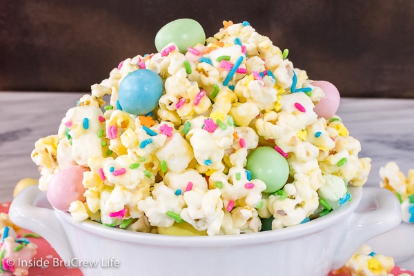 A close up picture of a white bowl filled with white chocolate popcorn with candy and sprinkles in it.