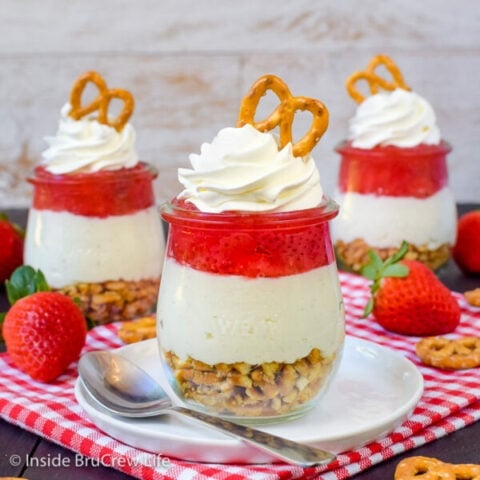 Three clear jars filled with strawberry pretzel salad on a white and red towel.