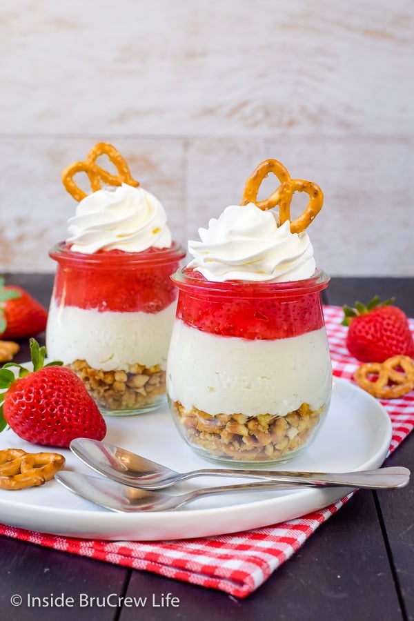 Two jars of strawberry pretzel salad on a white plate with two spoons beside them.