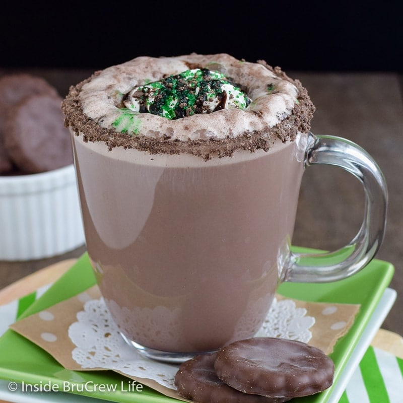 A clear mug full of a chocolate mint latte on a green plate.