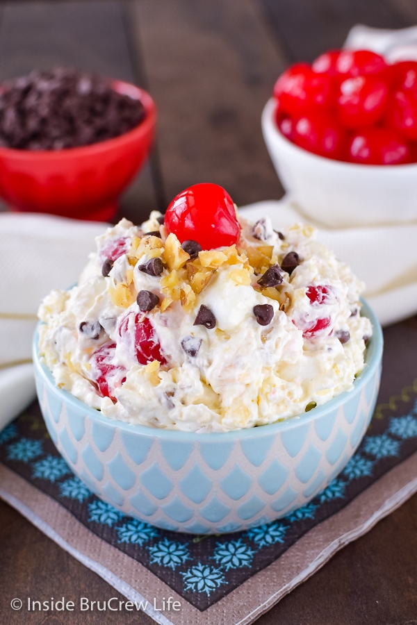 A white and blue bowl filled with banana split salad and topped with nuts, chocolate chips, and a cherry