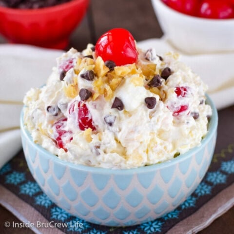 A blue and white bowl filled with banana dessert salad and topped with nuts, chocolate chips, and cherries