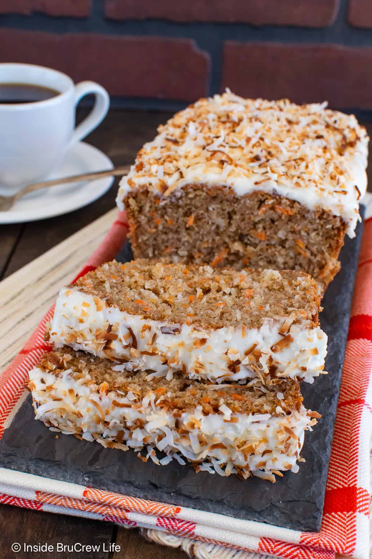 A loaf of carrot bread with frosting on a tray with two slices laying in front.