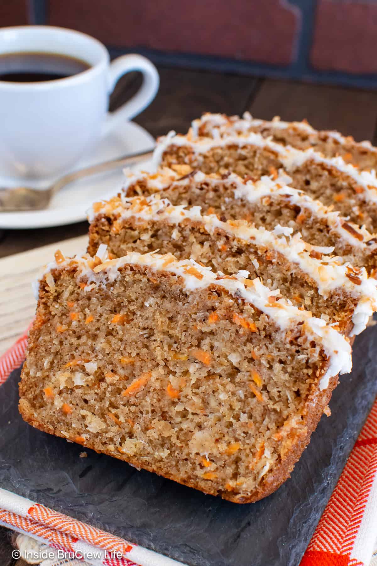 Slices of frosted carrot cake bread laying on a black tray.