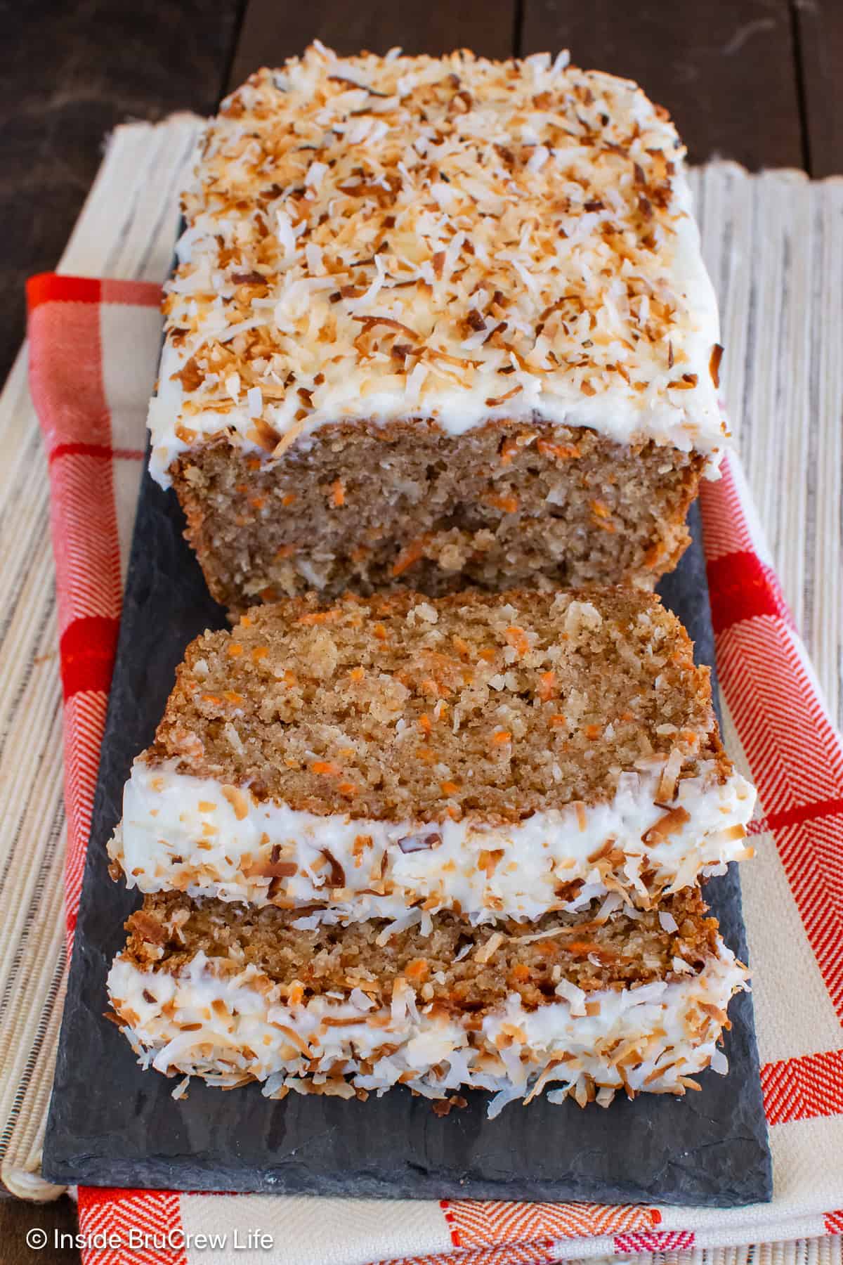 A loaf of carrot cake bread with frosting on a tray with two slices laying in front.