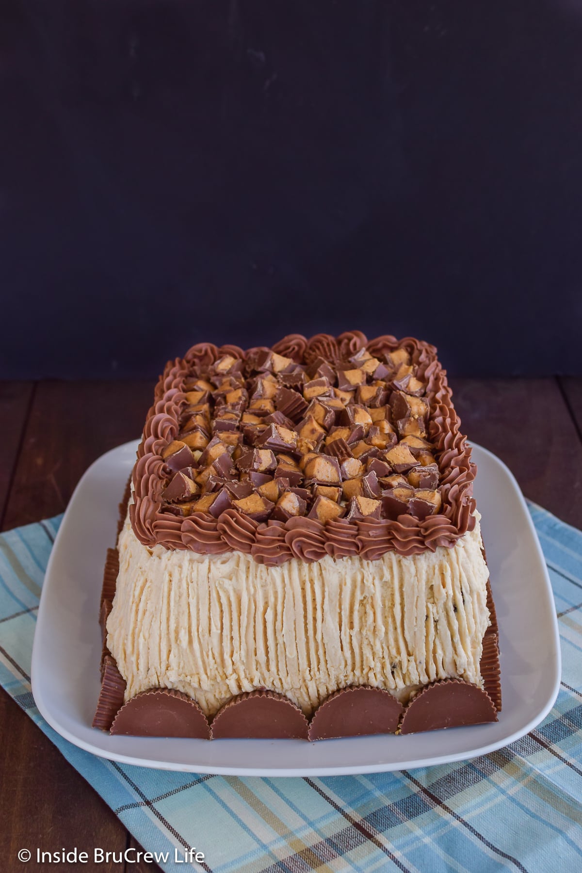 A frosted cake on a plate with chopped peanut butter candies on top.
