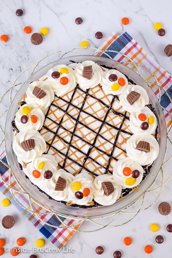 Picture of the top of a peanut butter pie topped with cool whip, peanut butter drizzles, and Reese's candies.