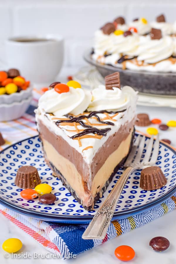 A piece of no bake peanut butter pie topped with chocolate pudding, Cool Whip, and Reese's candies on a blue plate