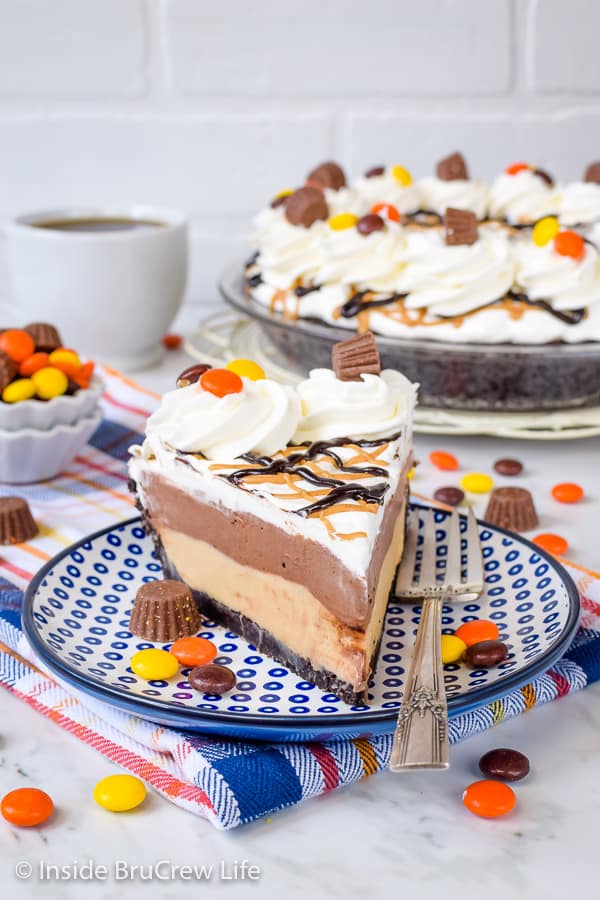 A blue plate with a slice of no bake pie with layers of peanut butter and chocolate pudding topped with Cool Whip.