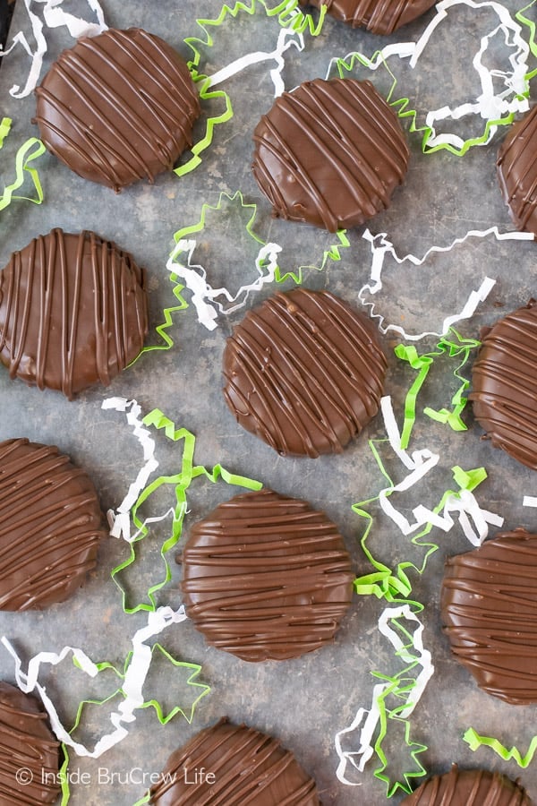 Chocolate covered coconut patties on white parchment paper surrounded by green and white paper pieces.