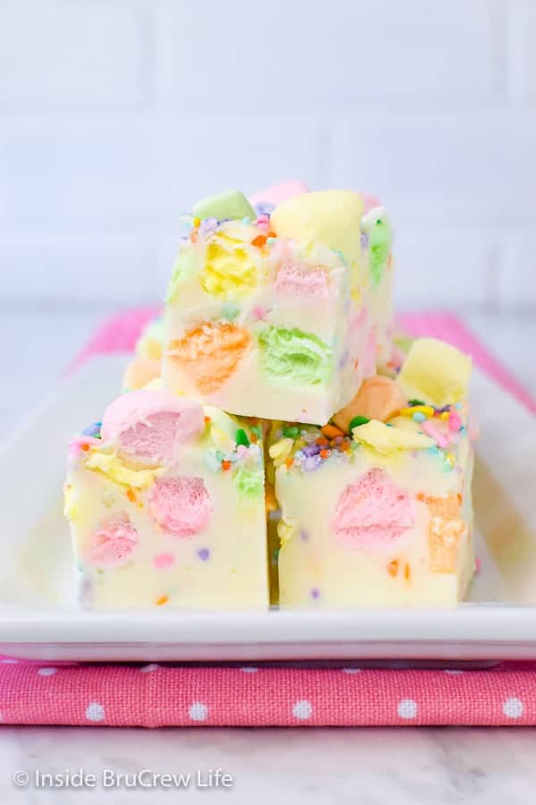 3 pieces of white fudge loaded with colorful marshmallows on a white plate on a pink polka dot napkin.