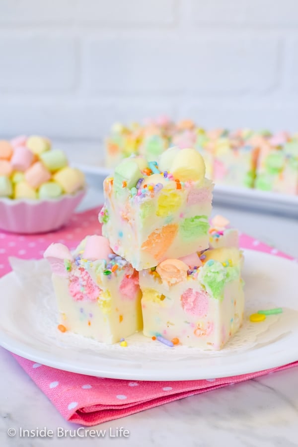 3 pieces of white fudge loaded with colorful marshmallows on a white plate on a pink polka dot napkin.