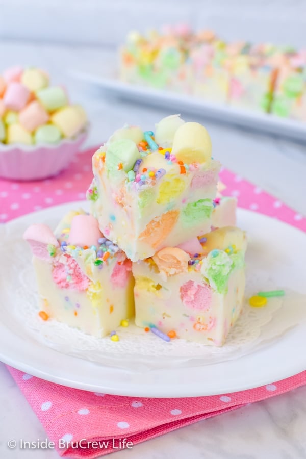 3 pieces of white fudge loaded with colorful marshmallows on a white plate on a pink polka dot napkin.