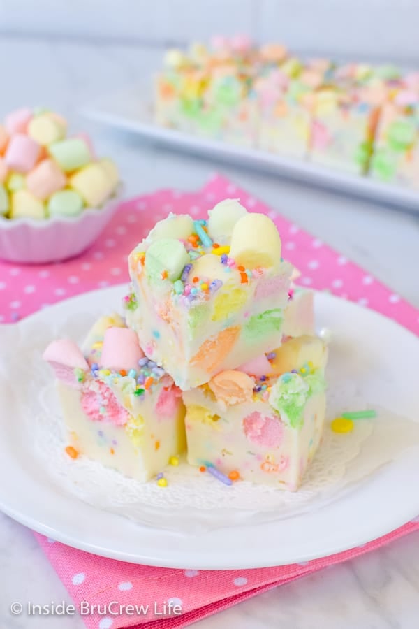 3 pieces of white fudge loaded with colorful marshmallows on a white plate on a pink polka dot napkin.