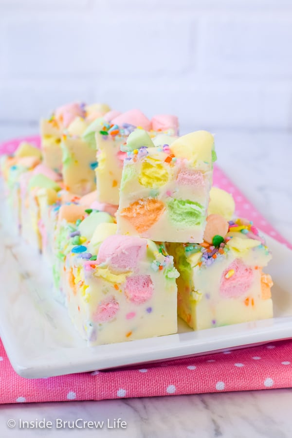 Multiple pieces of white fudge loaded with colorful marshmallows on a white plate on a pink polka dot napkin.