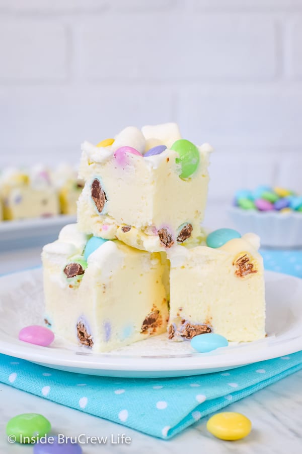 3 pieces of white fudge loaded with marshmallows and chocolate candies on a white plate on top of a blue polka dot napkin.